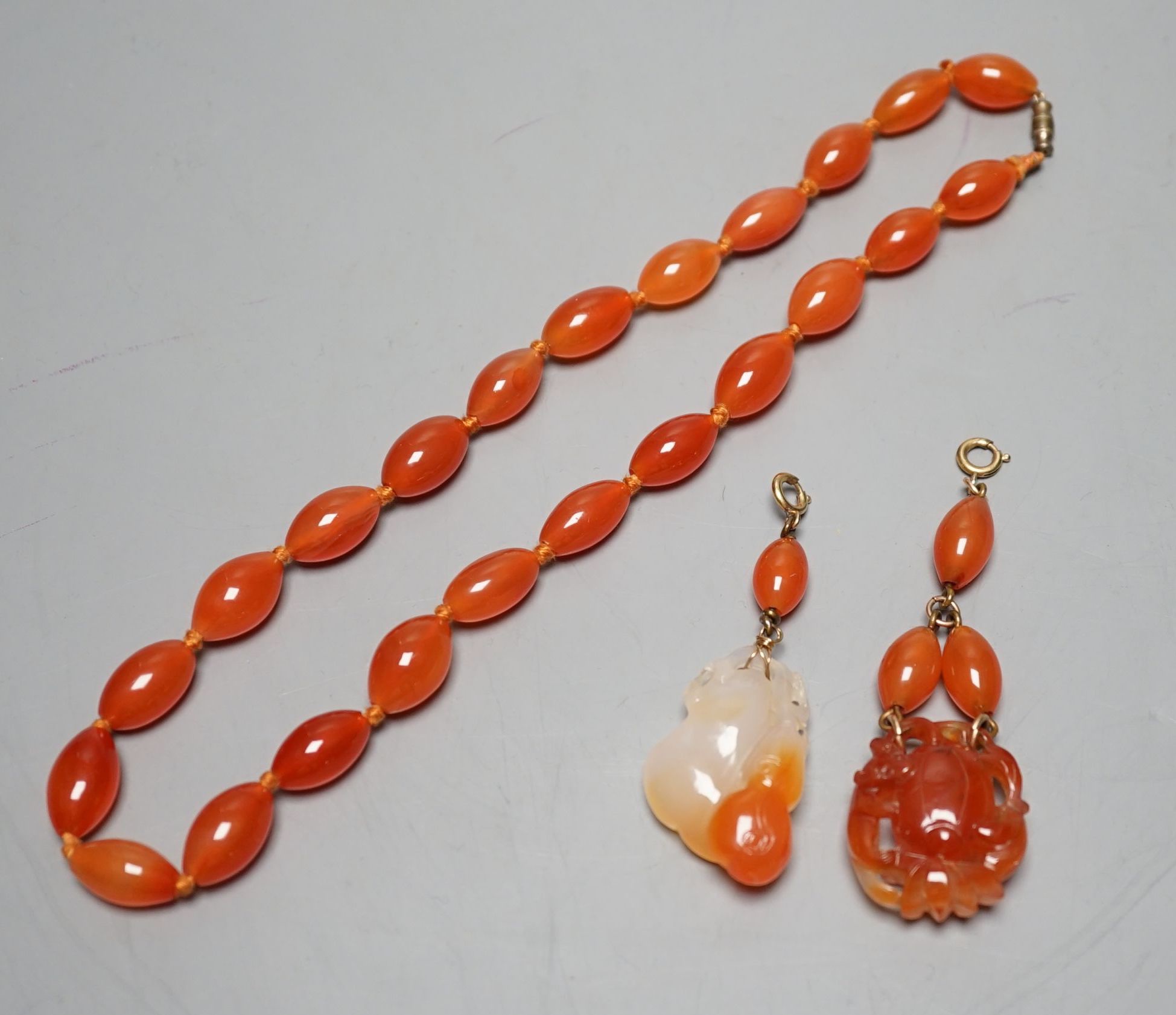 Two carved agate and carnelian bead pendants and a carnelian bead necklace, 48cm.